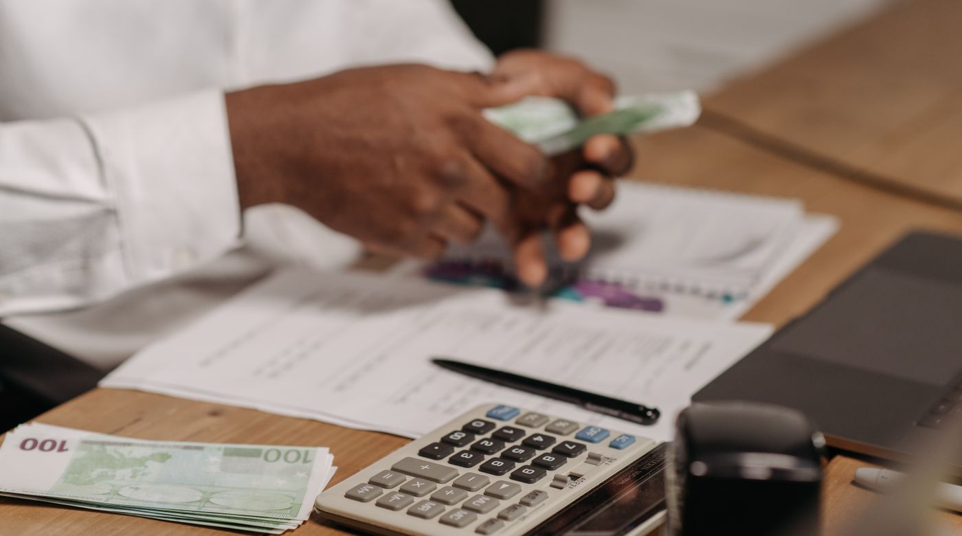 Des mains comptent des billets à côté d’une calculatrice